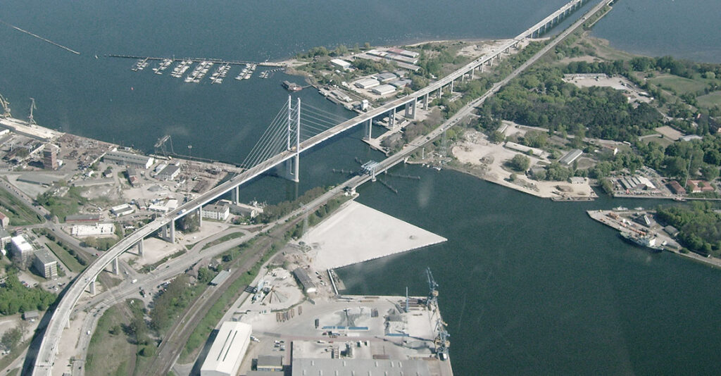 Luftaufnahme einer Brücke, die über einen Wasserweg führt, mit Booten im Hintergrund.
