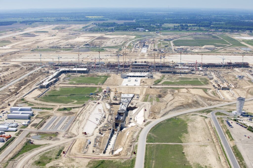 Luftaufnahme einer Baustelle mit verschiedenen Bauarbeiten und Maschinen auf einem großen Gelände.