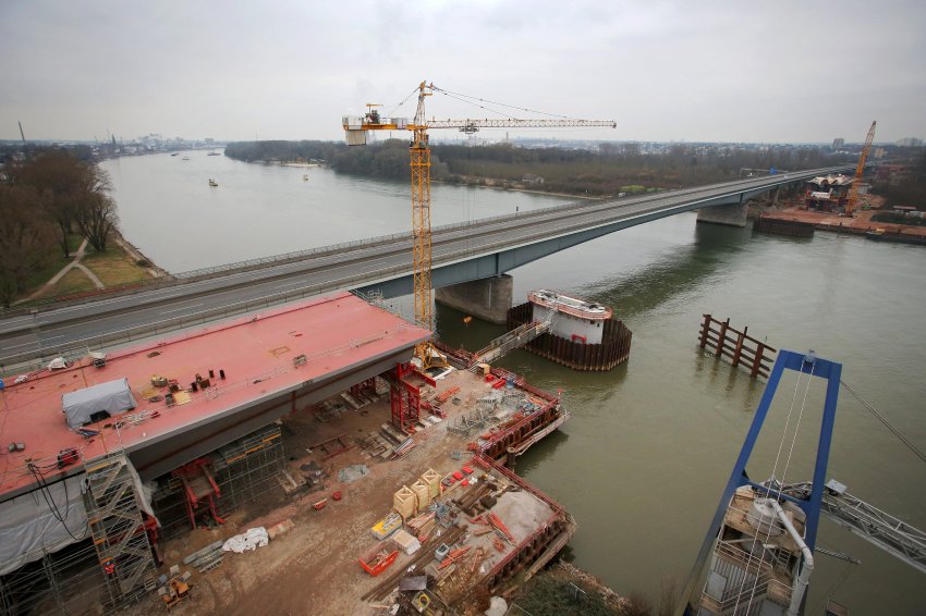 Bauarbeiten an einer Brücke mit einem Kran und einem Fluss im Hintergrund.