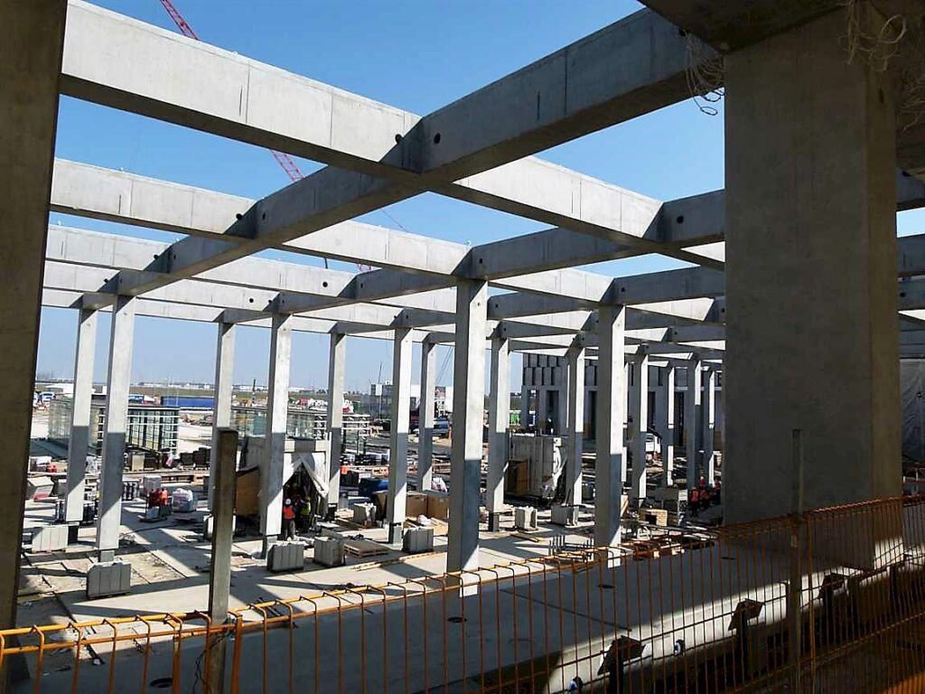 Baugerüst mit sichtbaren Betonstützen und Baustellenaktivitäten im Hintergrund.