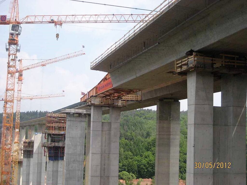 Bau einer Brücke mit Kränen und Betonpfeilern auf einer Baustelle.