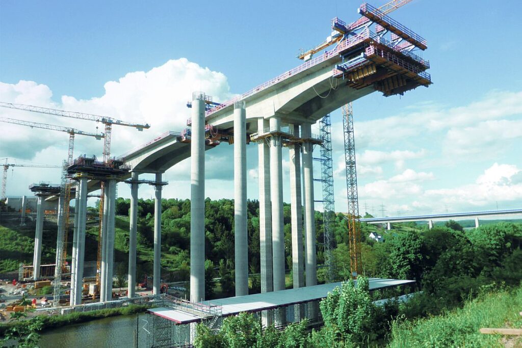 Brücke im Bau mit Betonpfeilern und Baukränen auf einer Baustelle.