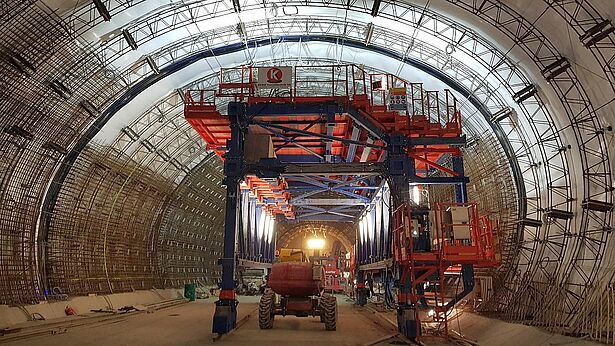 Baugerüst und Maschinen in einem Tunnel während der Bauarbeiten, beleuchtet von starken Scheinwerfern.