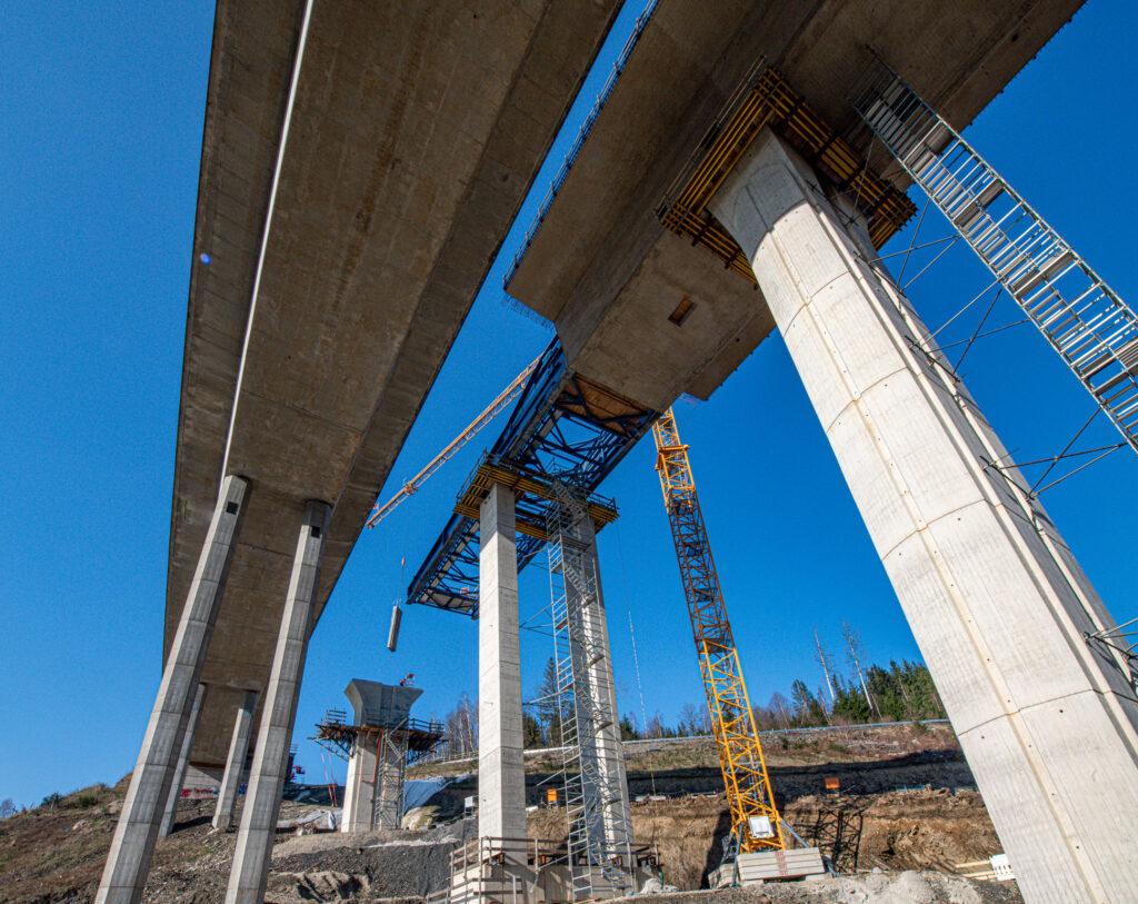 Bauarbeiten an einer Brücke mit Betonpfeilern und Stahlgerüsten unter klarem Himmel.