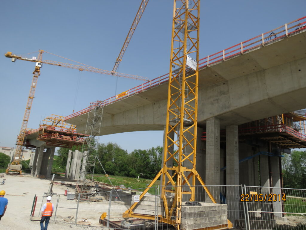 Bauarbeiten an einer Brücke mit Kränen und Baugeräten auf einer Baustelle.