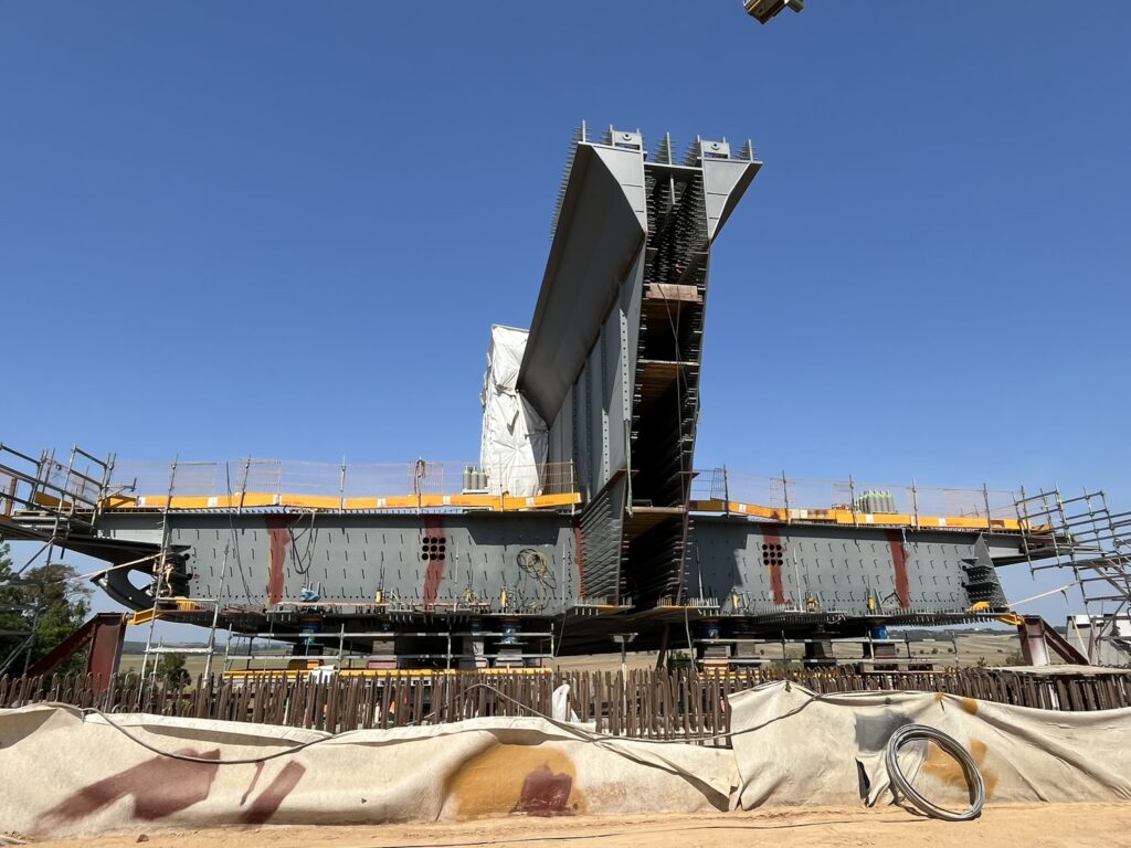 Bau eines großen Brückenabschnitts mit Stahlkonstruktion und Baugerüst unter klarem Himmel.