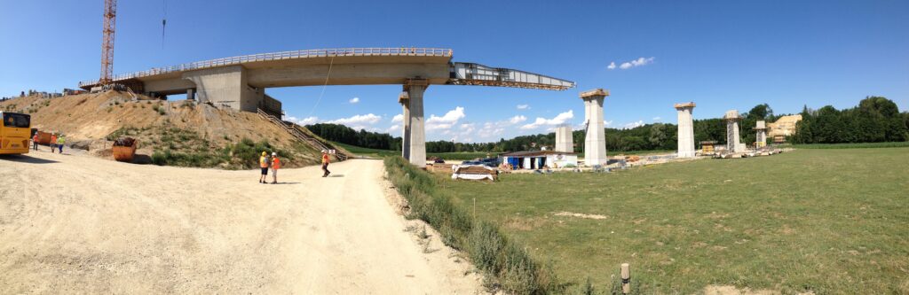 Bau einer Brücke mit mehreren Pfeilern und einem Kran im Hintergrund auf einer Baustelle.