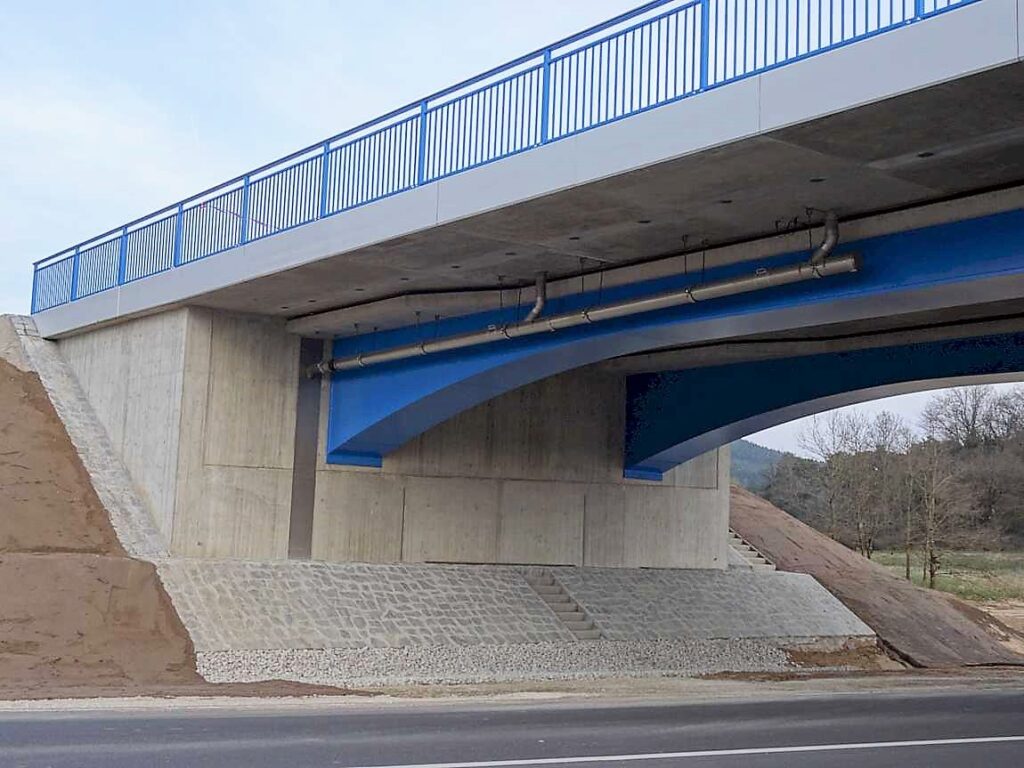 Brücke mit blauen Akzenten und Betonunterbau, sichtbar von der Seite.