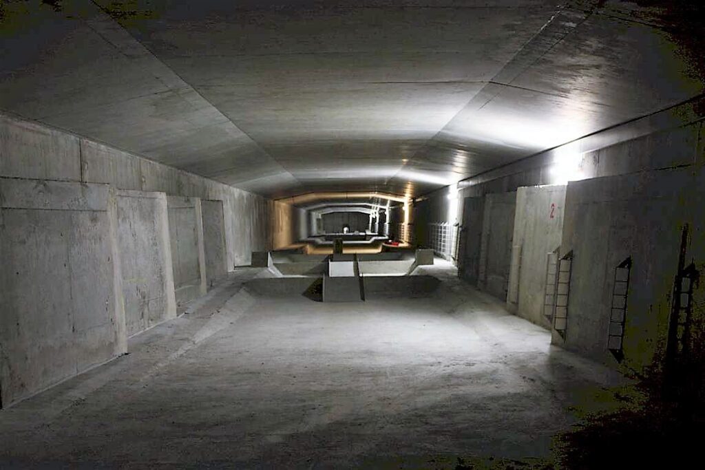 Blick auf einen langen, betonierten Tunnel mit gleichmäßiger Beleuchtung und strukturierten Wänden.