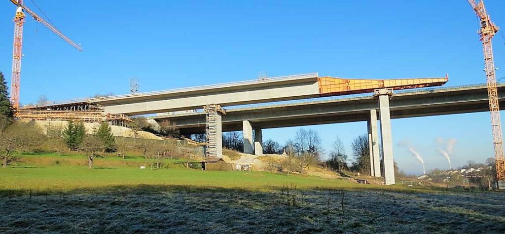 Bau einer Brücke mit Betonpfeilern und Kränen unter blauem Himmel.